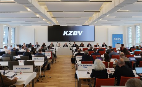 Heller Saal mit Menschen in parlamentarischer Bestuhlung mit Leinwand KZBV-Schriftzug