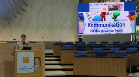 Frau spricht an Pult, im Hintergrund große Präsentationsleinwand
