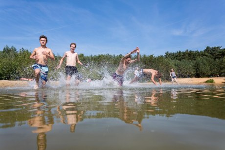 junge Männer laufen und springen in ein natürliches Gewässer