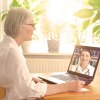 Ältere Patientin macht sich bei Online-Sprechstunde mit Ärztin am Tisch Notizen.