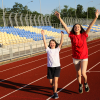 Zwei Mädchen, eines mit Down-Syndrom laufen jubelnd über Sportplatz