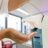 medizinisches Personal hält Hand unter Desinfektionsspender, der mit dem Ellbogen heruntergedrückt wird