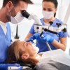 weibliche Patienten auf Zahnarzt-Behandlungsstuhl, Arzt schaut durch Vergrößerungshilfe in Mundbereich