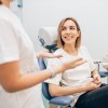lächelnde Patientin im Zahnarztstuhl, neben ihr Ärztin, die etwas zu erklären scheint