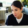 Frau in Kleidung von medizinischem Personal schaut konzentriert nach unten rechts, vermutlich auf Computer