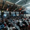 große Halle mit Sitzreihen mit Publikum und Bühne mit Redner und Präsentation
