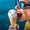 Frau mit Sonnenbrille vor blauem Hintergrund schleckt an einer Kugel Eis im Hörnchen
