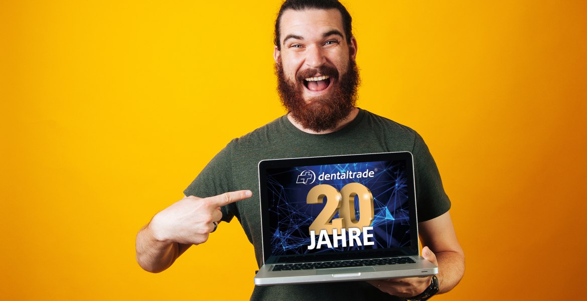 Freudestrahlender Mann hält Laptop in der Hand mit Logo "dentaltrade 10 Jahre" vor orangenem Hintergrund