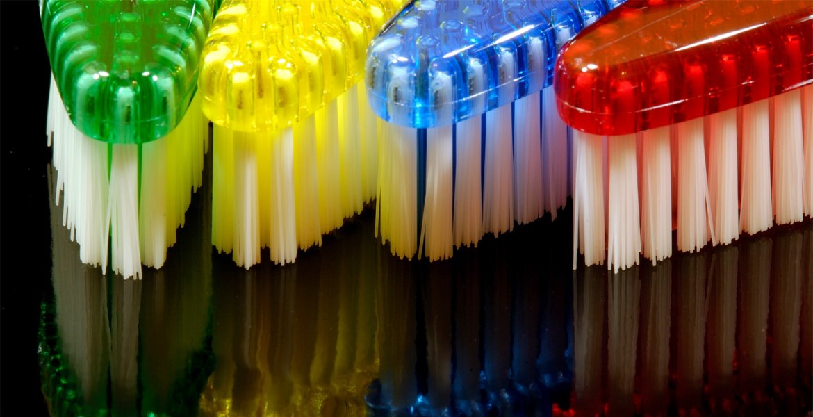 bunte Zahnbürstenköpfe sich spieglend auf schwarzem Untergrund