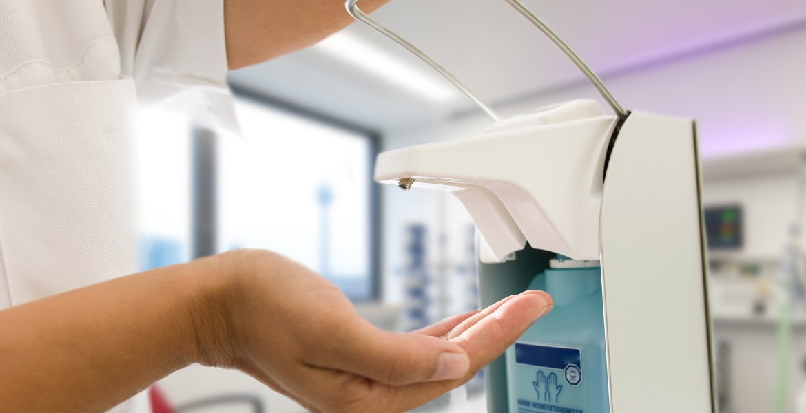medizinisches Personal hält Hand unter Desinfektionsspender, der mit dem Ellbogen heruntergedrückt wird