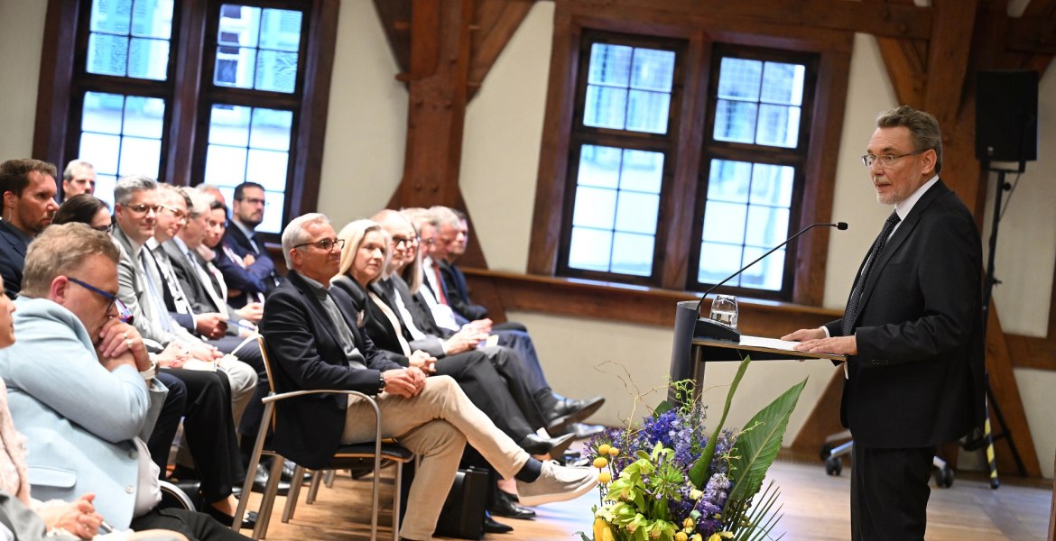 sitzendes Publikum, festlich geschmückter Raum, ein Mann spricht am Podium