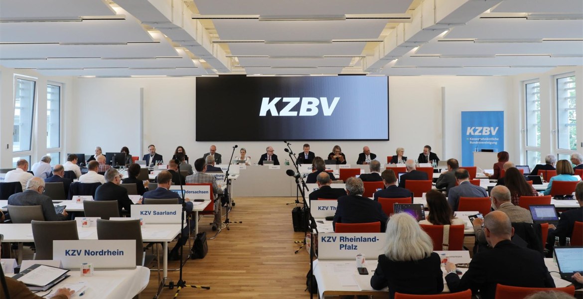 Heller Saal mit Menschen in parlamentarischer Bestuhlung mit Leinwand KZBV-Schriftzug