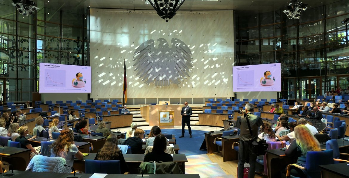 großer Plenarsaal mit Bundesadler an der Wand, ein Mann steht in der Mitte und spricht