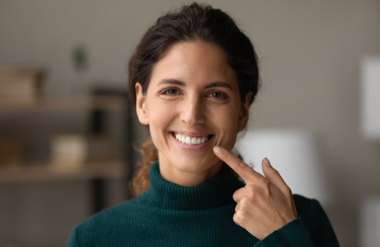 Ein Bild, das eine junge, lächelnde, dunkelhaarige Frau zeigt, die mit einem Finger ihrer Hand auf ihre Zähne zeigt