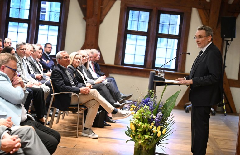 sitzendes Publikum, festlich geschmückter Raum, ein Mann spricht am Podium