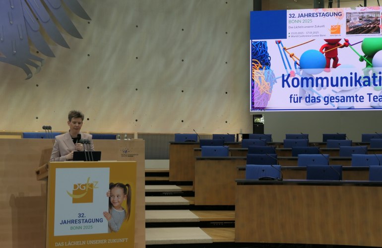 Frau spricht an Pult, im Hintergrund große Präsentationsleinwand