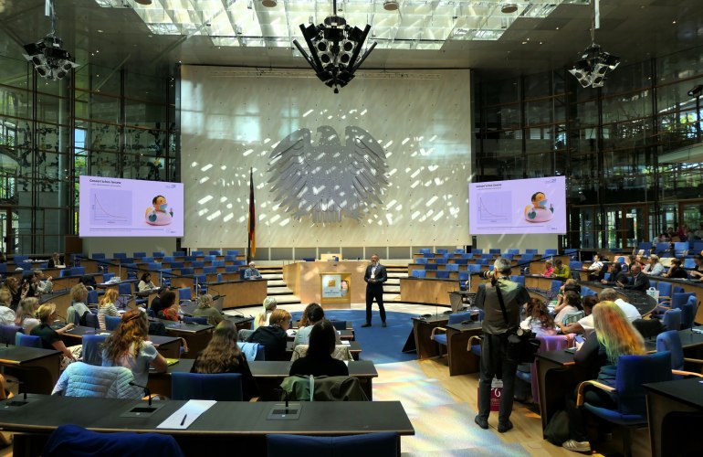 großer Plenarsaal mit Bundesadler an der Wand, ein Mann steht in der Mitte und spricht